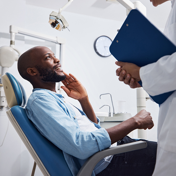 Man touching his face while talking to his dentist