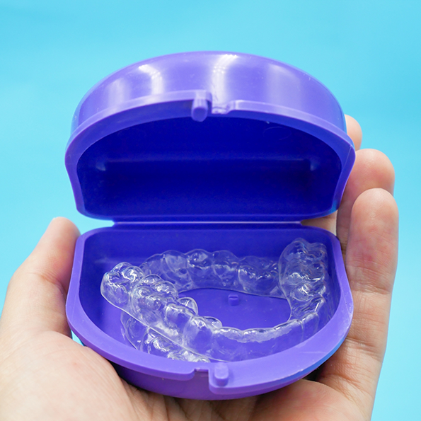 Hand holding a blue plastic case with two clear aligners