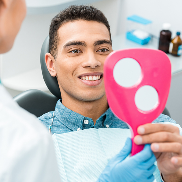 Man in dental chair looking at his smile in a mirror