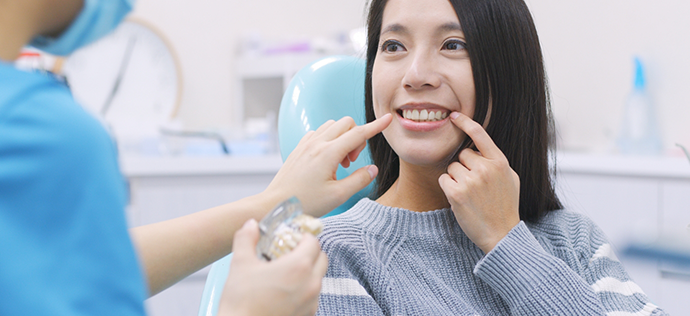 Woman in dental chair pointing to her smile