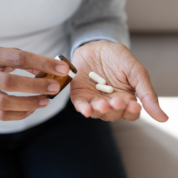 Person taking two white pills out of a pill bottle