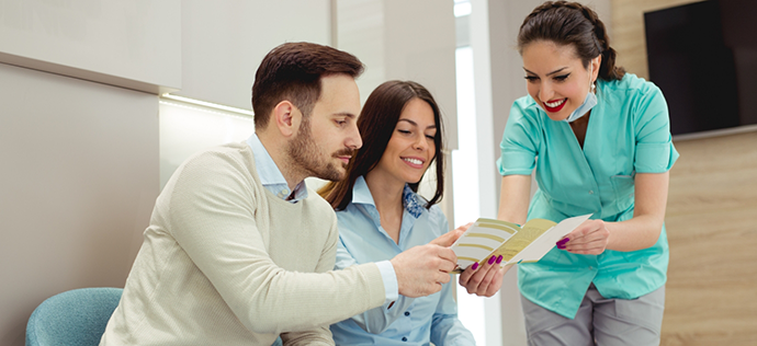 Dental team member showing a pamphlet to two patients