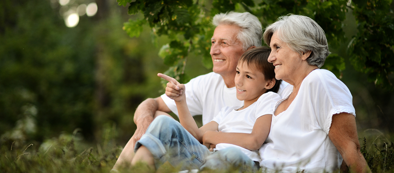 Child sitting with their grandparents near green trees